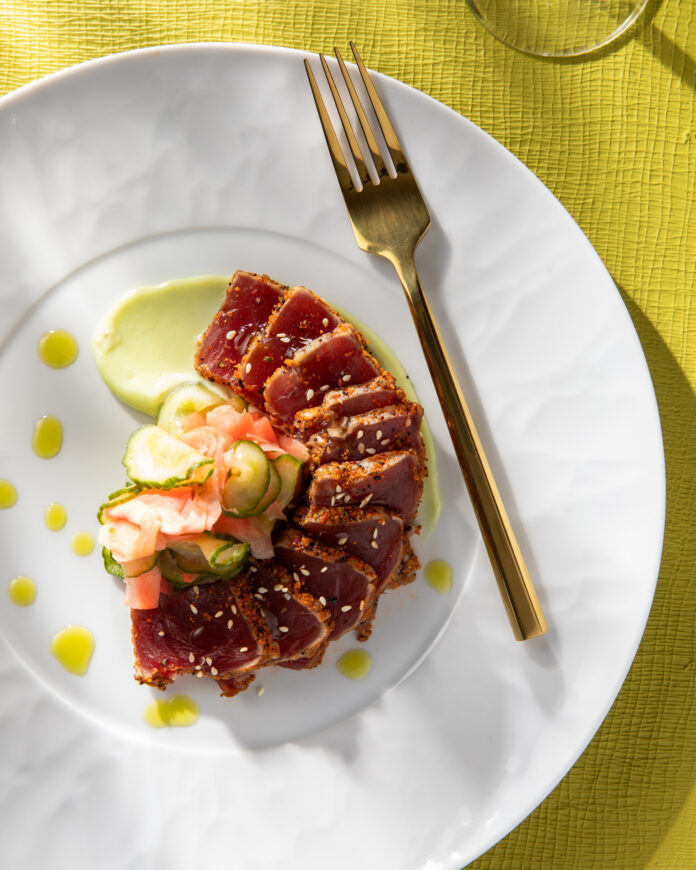 An above shot of a seafood dish, served on a white plate with a gold fork on the right side of the meal.