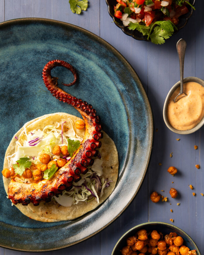 An above shot of an octopus taco laying on a blue plate.