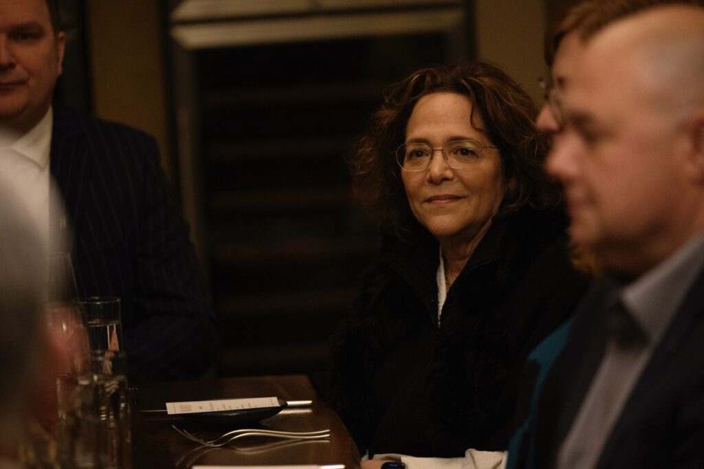 A woman in a black jacket and dark curly hair listens to other Downtown Pittsburgh businesspersons speak.