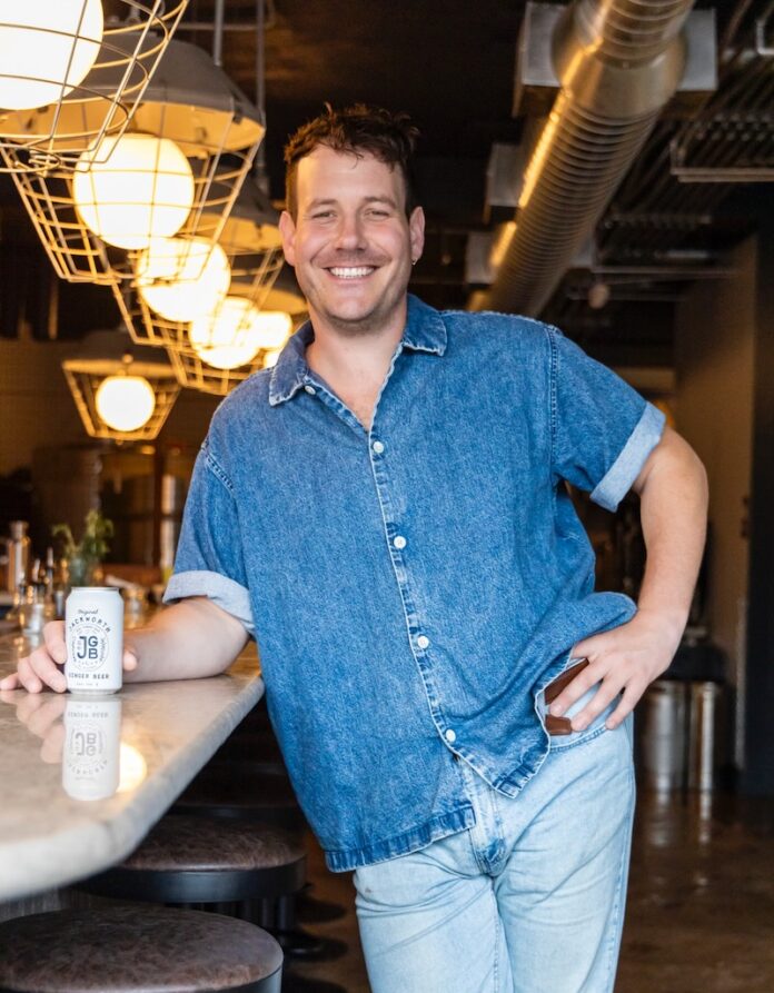 A man in a blue jean shirt and light jeans stands at a bar as a fun thing to do in Pittsburgh.