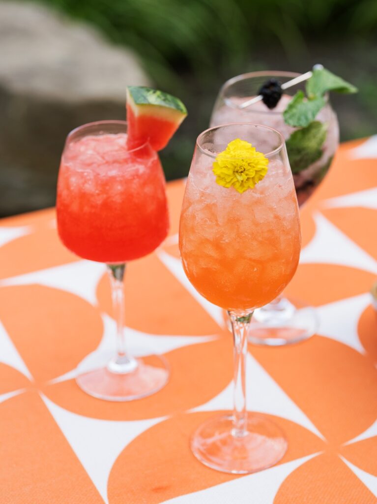 Three glasses each with a garden-fresh spritz with watermelon, flower, and blackberry garnishes.