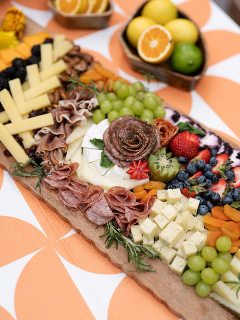 A charcuterie board with meats, cheese, and fruit sit on an orange picnic table.