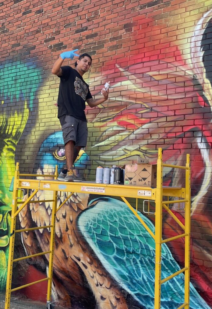 Explore the Graffiti of Pittsburgh A graffiti artist in Pittsburgh poses for the camera in front of his spray painted blue bird.
