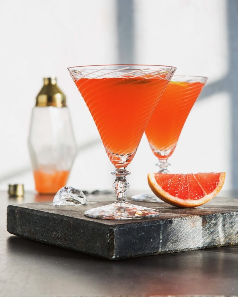 Two Gypsy Eyes Green Chartreuse and gin cocktails sit on a dark marble block beside a slice of grapefruit.