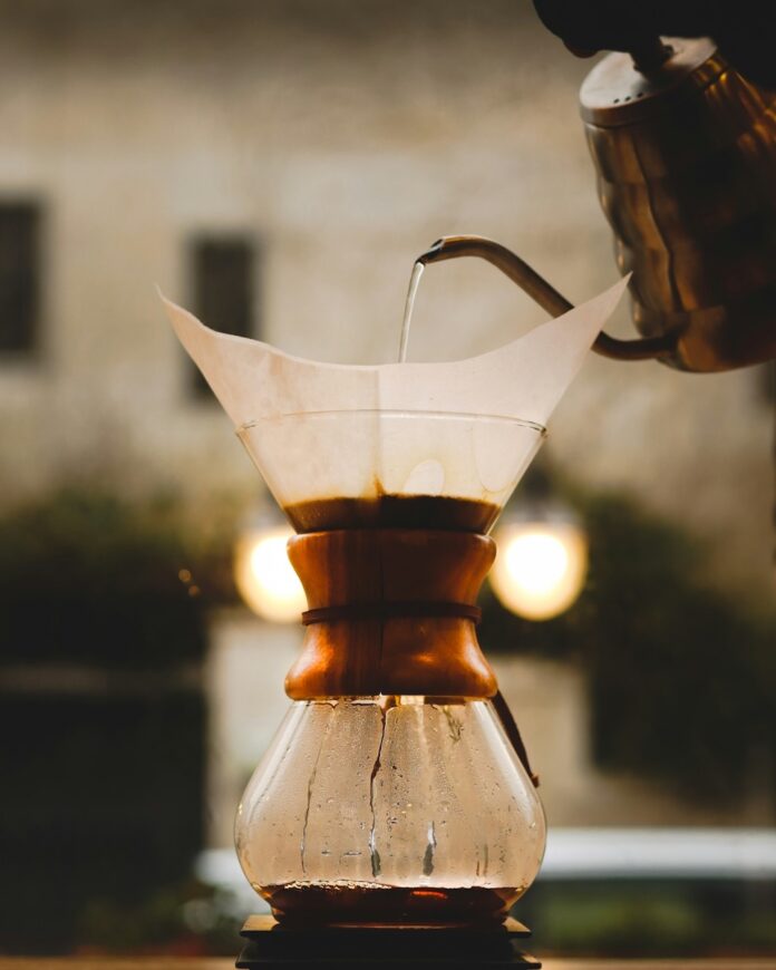 A person brews coffee at home with a pour-over method using a kettle and coffee pot and filter.