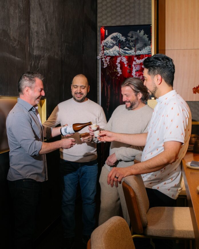 Four men cheers as one pours each of them a small glass of liquor.