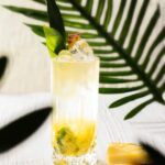 A tall tropical cocktail for Jurassic World: Rebirth with pineapple leaves and mint for garnish, hidden amongst jungle palms.