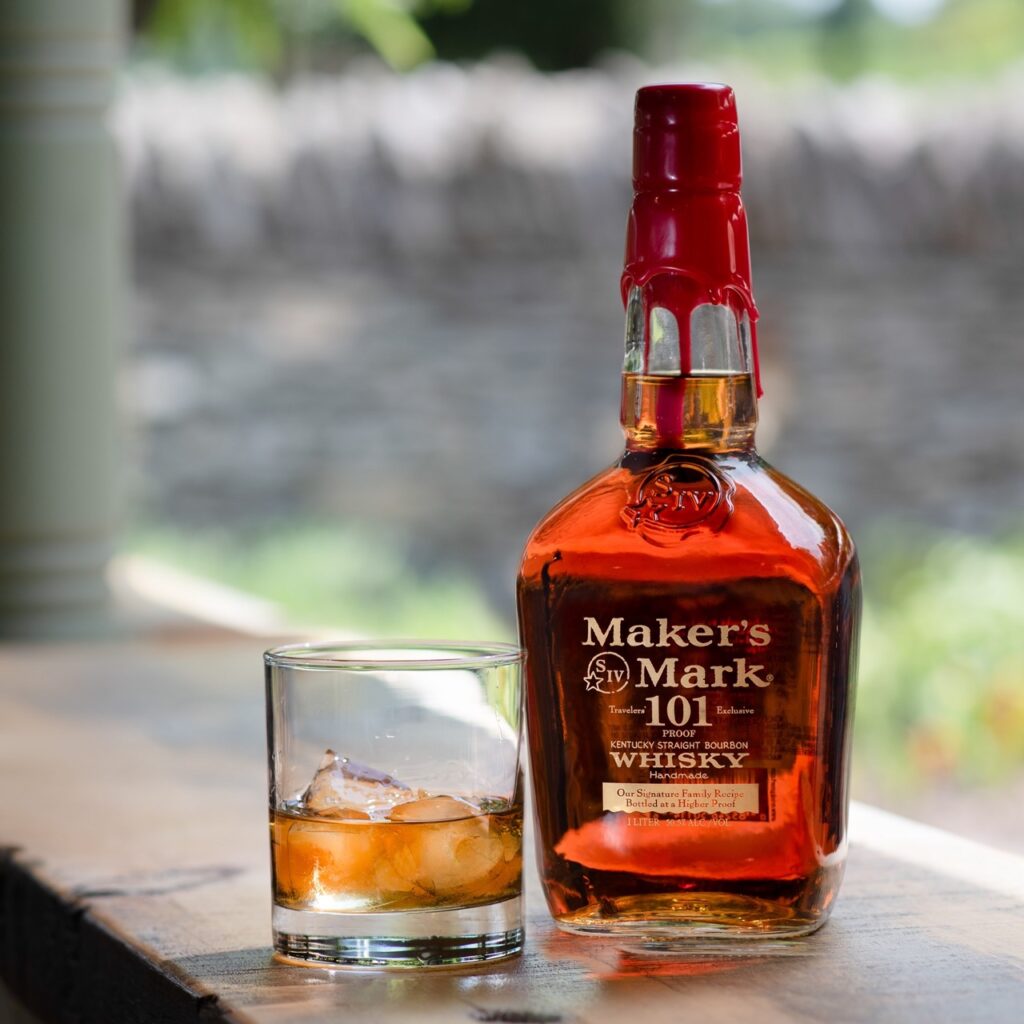 A bottle of Maker's Mark 101 sits beside a glass of whiskey with ice in it.