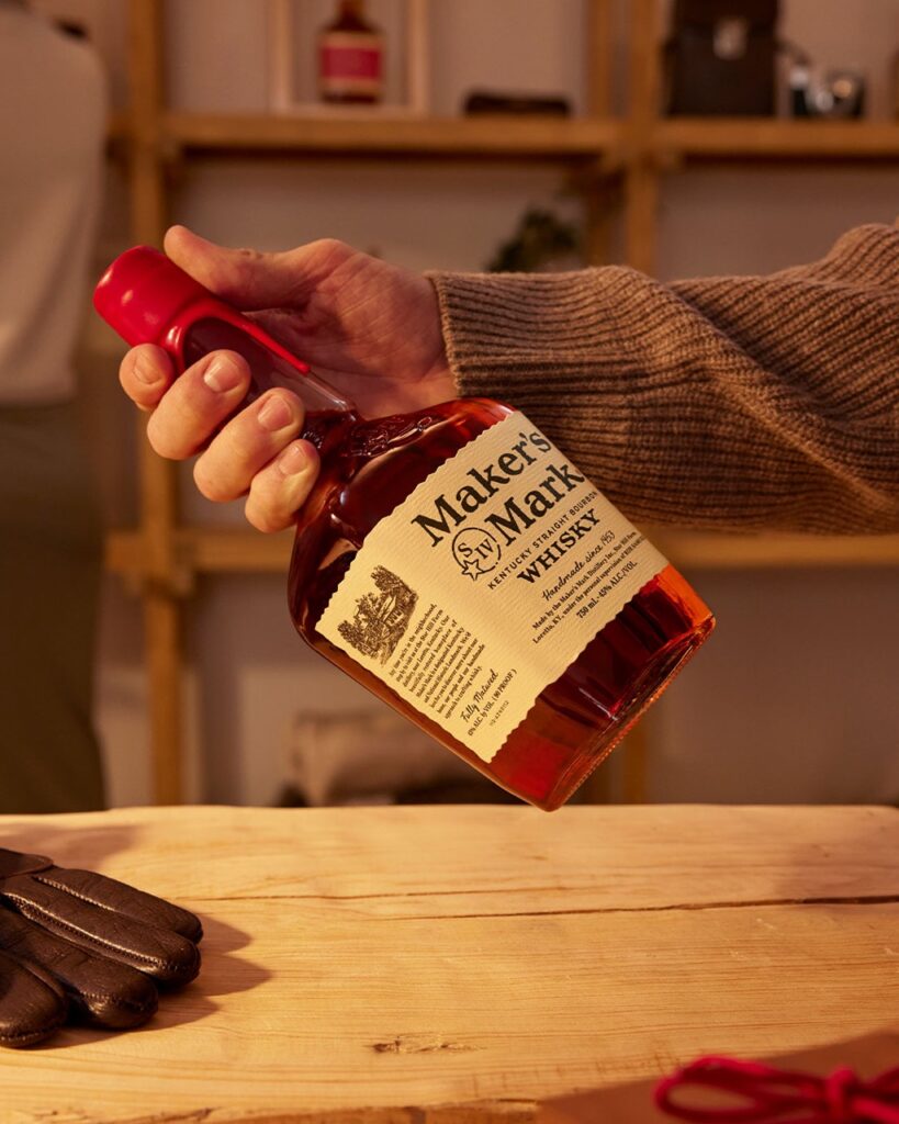 A bottle of Maker's Mark whiskey for Father's day that a dad in a sweater is holding to look at the label.