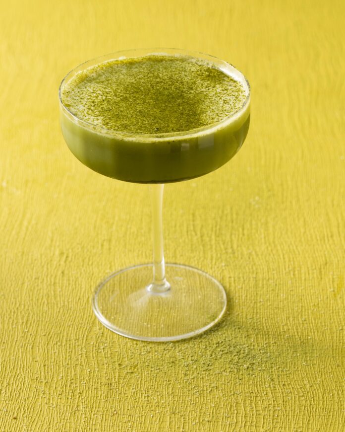 A coupe glass full of a green matcha martini with matcha powder on top all on the green background.