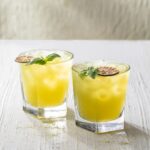 Two glasses hold a Matcha Mule with a lime wheel and sprig of mint on top of the glasses all on a white background.