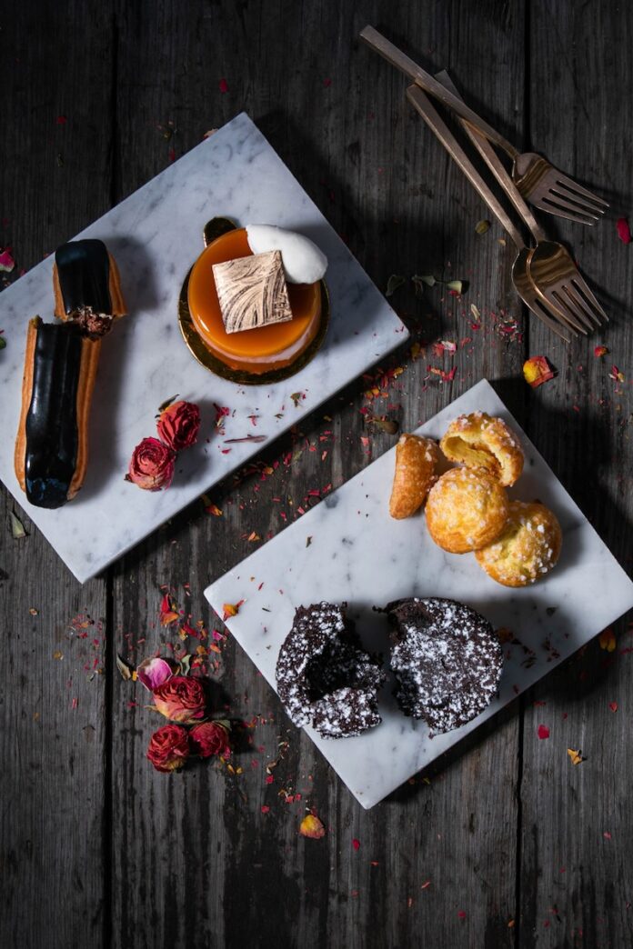 Various French dessert pastries sit on two white plates on a wooden table.