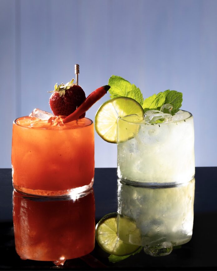 A red light and green light cocktail for Squid Game sit beside each other on a black mirror background.