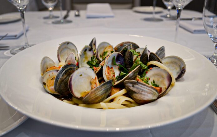 Linguini and clams in a white bowl on a set table.