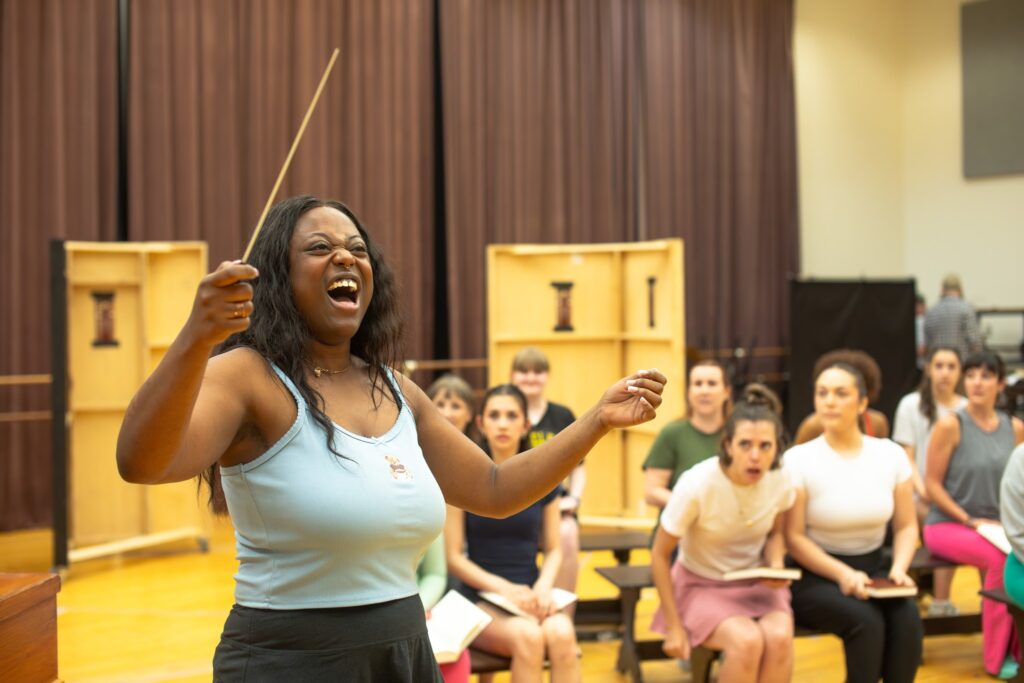 A woman in a tank top conducts other cast mates in a practice for Sister Act the Musical in Pittsburgh.