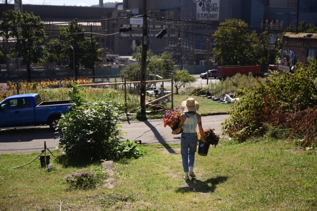 A woman carries pots of flowers down a hill in Braddock.