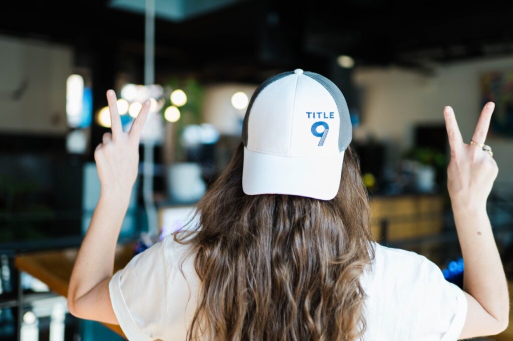 A woman with a backwards baseball cap on puts up two peace signs with her fingers.