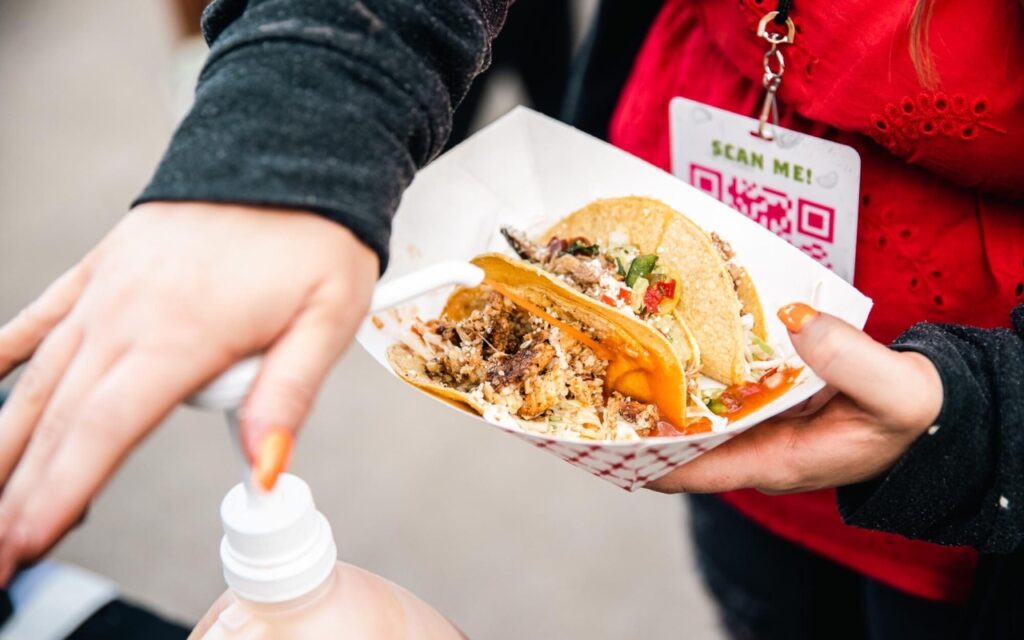 A person pumps a sauce onto their tacos in a food boat at Pittsburgh taco and tequila festival.