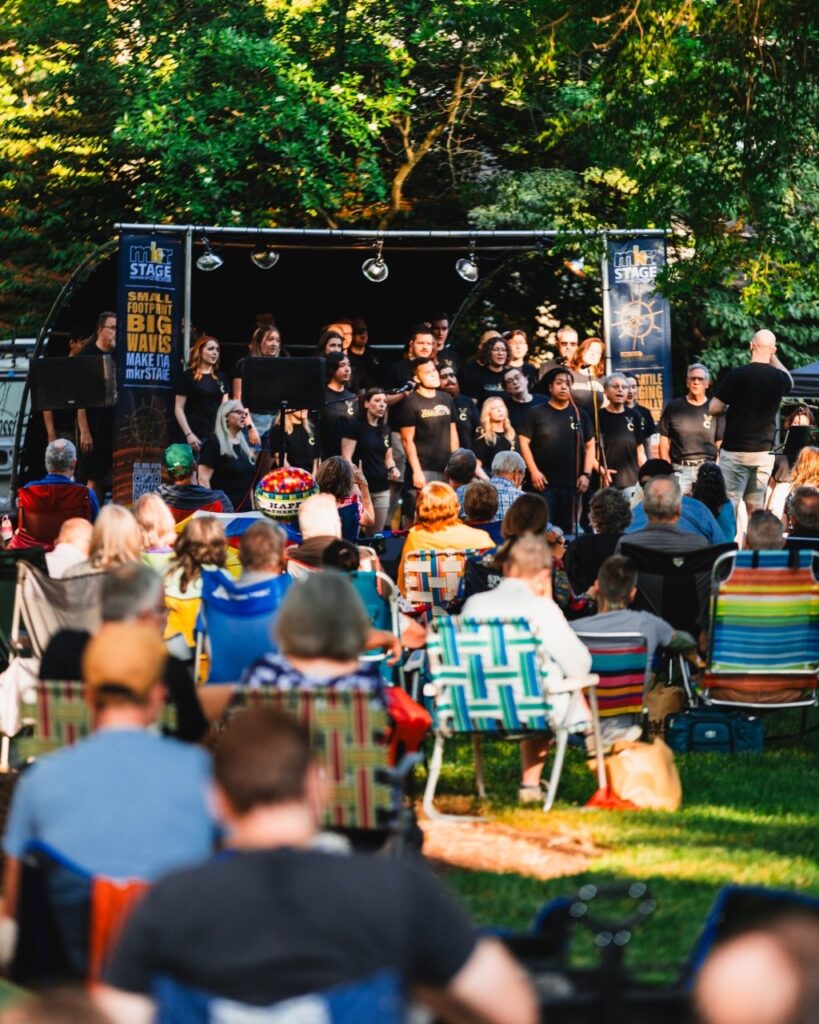 Groups of people sit on the lawn at the Frick in Pittsburgh to watch a band on a stage.