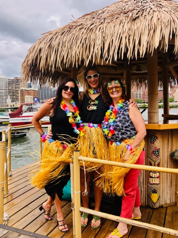 A tiki cruise boat on Pittsburgh's Three Rivers with three women in hawaiian attire together.