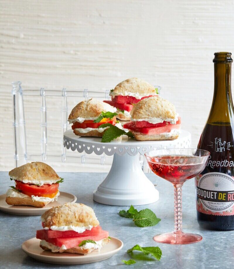 Three Watermelon Sandwiches served on a heightened plate. Two sandwiches served on two smaller plates on the side.