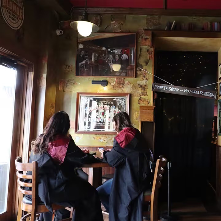 Two people in wizard robes sit at a table in a bar in Pittsburgh for a wizarding event. 