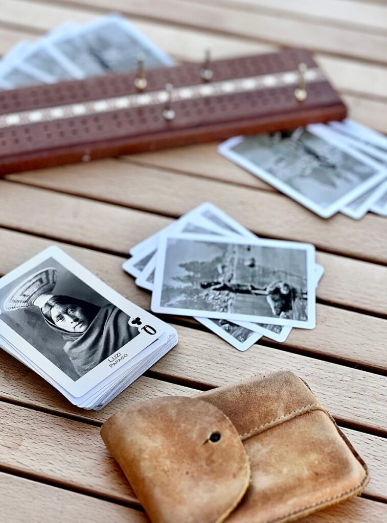 Several playing cards, featuring black and white portraits, are scattered around the board, and a small brown leather pouch is in the foreground.