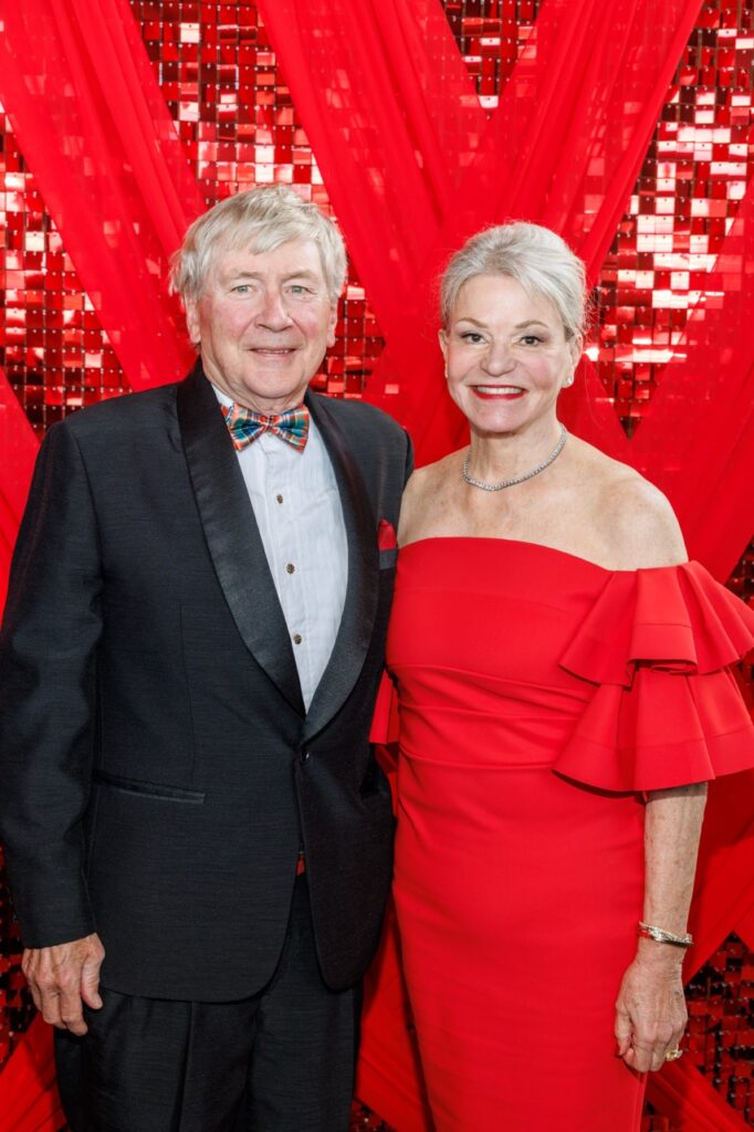 A man in a black suit and plaid tie stands witha. woman in a red dress.