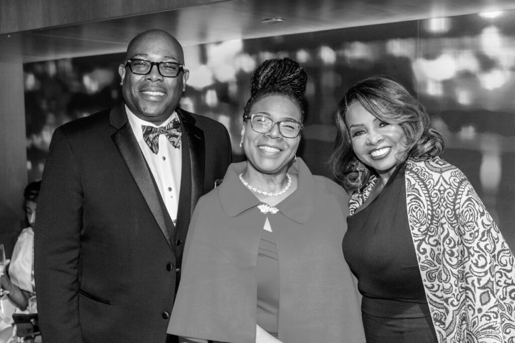 Two women and one man smile together in a black and white photograph.