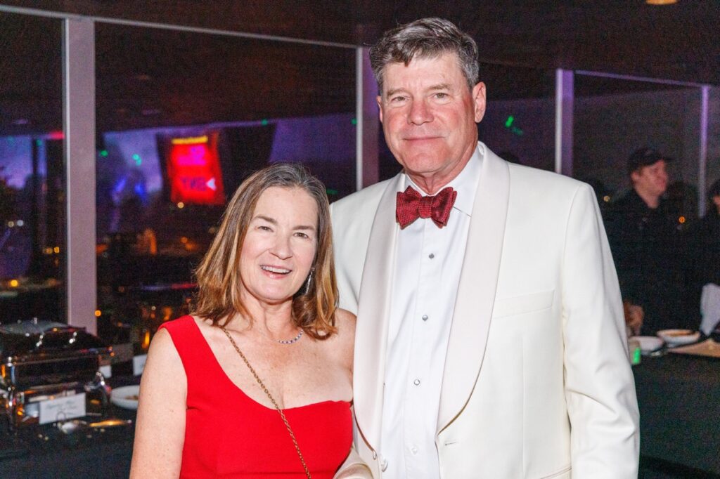 A woman in a red dress stands with a man in a white suit jacket and red bowtie.
