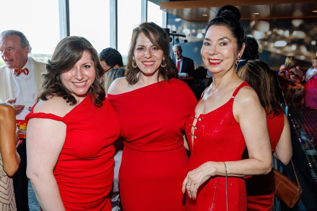 Three women in red dresses stand together.