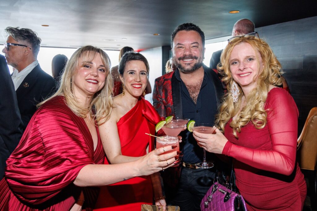 Three women in red and a man in a red and black suit jacket cheers red drinks.