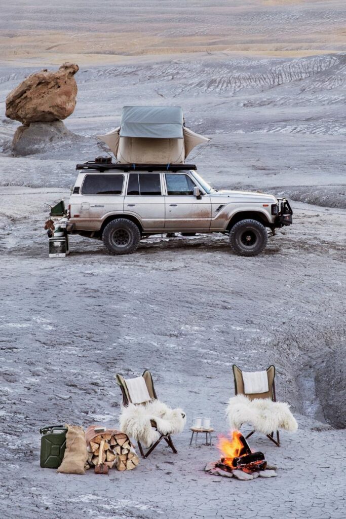 A light-colored SUV with a rooftop tent is parked in a desolate, rocky landscape.