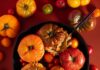 Baked Tomatoes Baked tomatoes, some with their tops removed and others still lidded, are arranged in a dark cast-iron skillet, surrounded by smaller, colorful cherry tomatoes and green herbs.