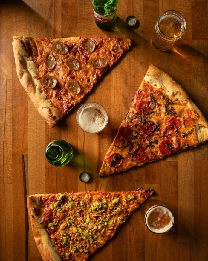 An above shot of three large slices of pizza on a wooden cutting board.