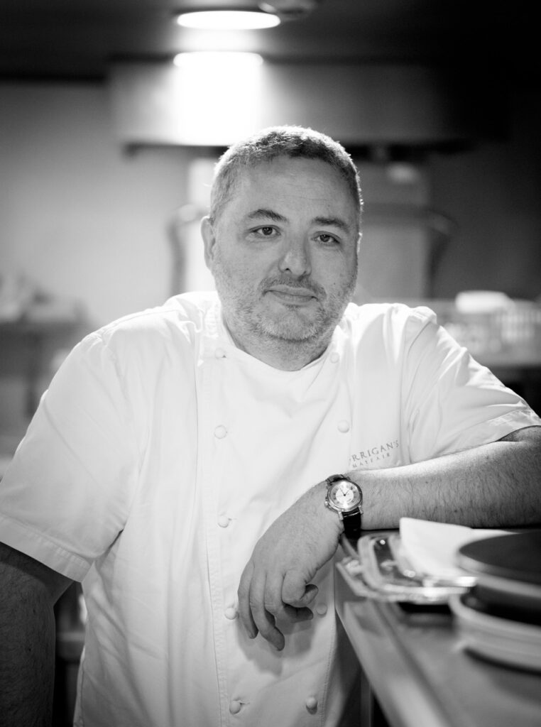 Chef Richard leans on a stack of plates in the Bentley's kitchen in London.