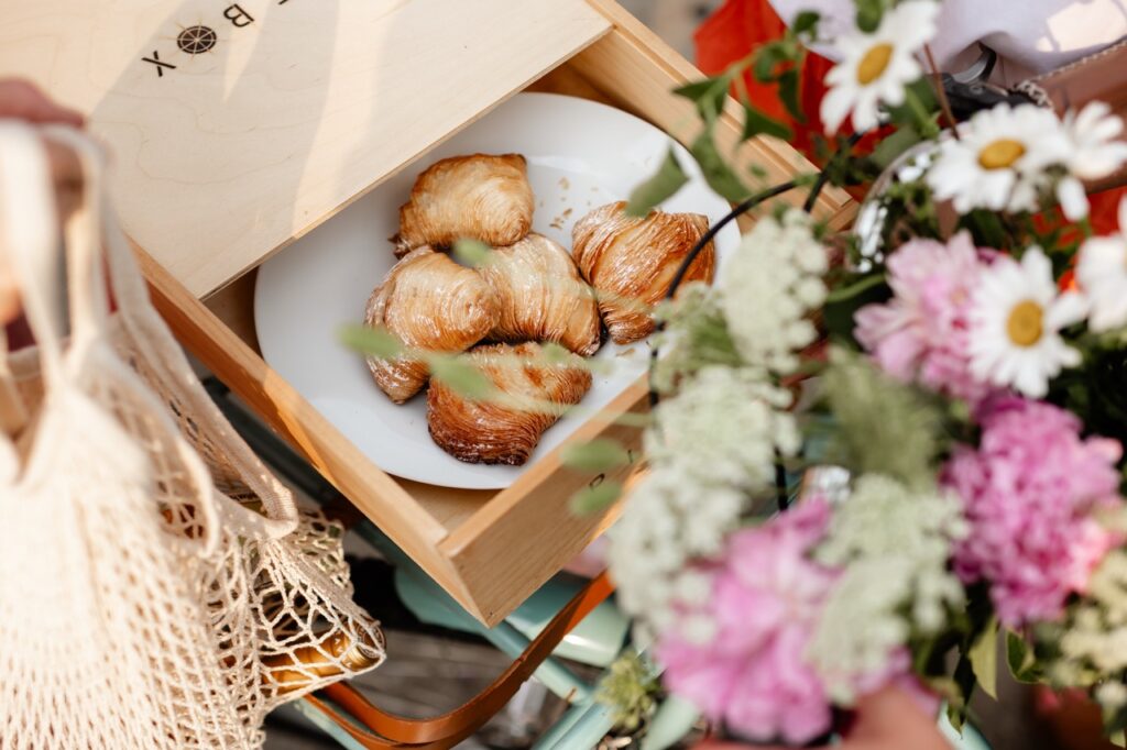 A box of croissant pastries next to a bundle of flowers on a bike.