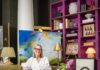 Layered Living at Brenda Friday Design’s Shoppe B Brenda Friday sits in a chair in her Shoppe B space with paintings around her and decor everywhere.