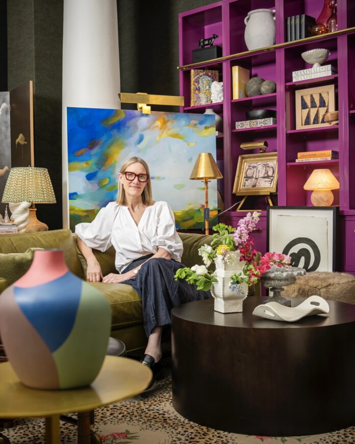 Brenda Friday sits in a chair in her Shoppe B space with paintings around her and decor everywhere.