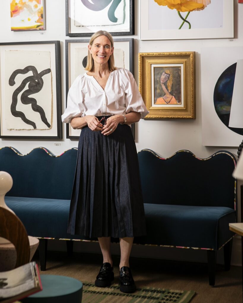 Brenda Friday stands in front of a wall of framed photos and a blue couch.