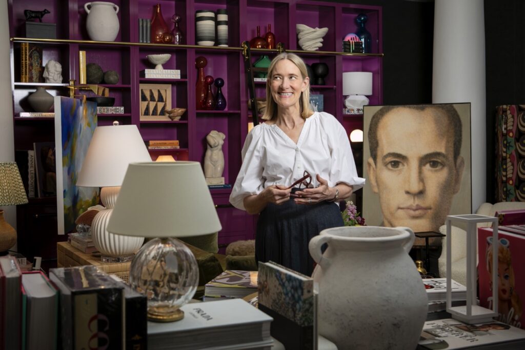 Brenda Friday stands in her Shoppe B area with a purple shelf of items behind her and lamps everywhere.