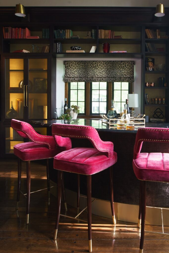 Three pink chairs sit at a bar with rectangular windows in the distance.
