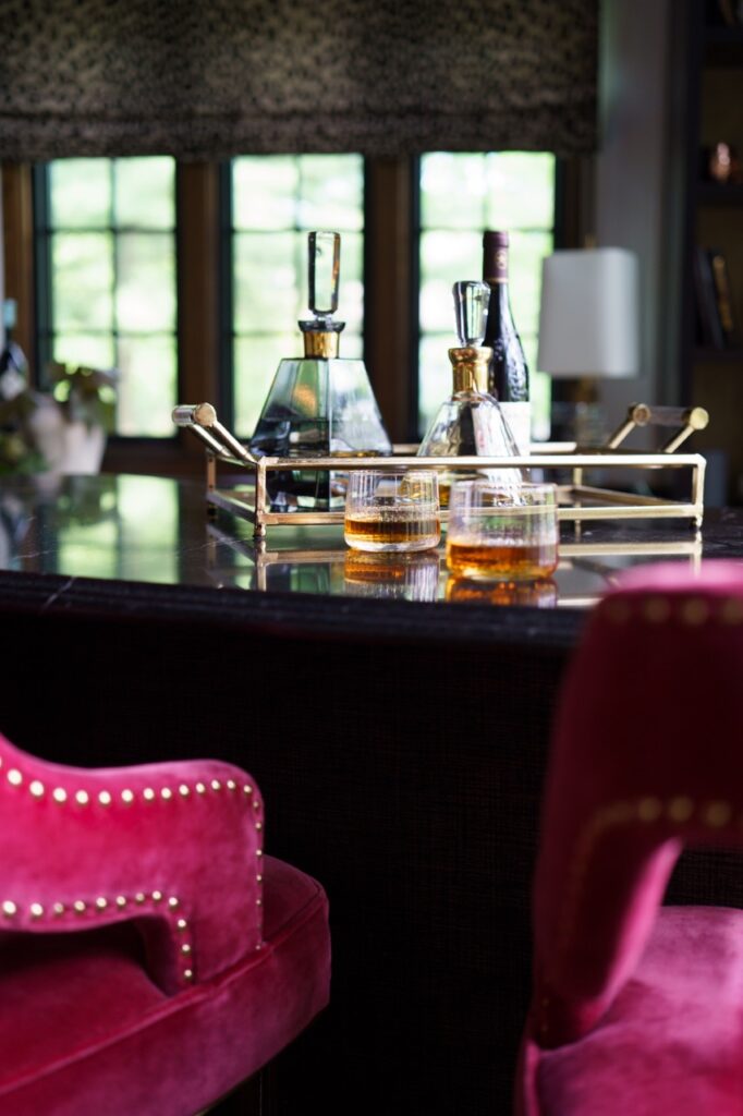 A close up of the a bar with a gold basket and two drinks on it as well as two pink chairs beside it.