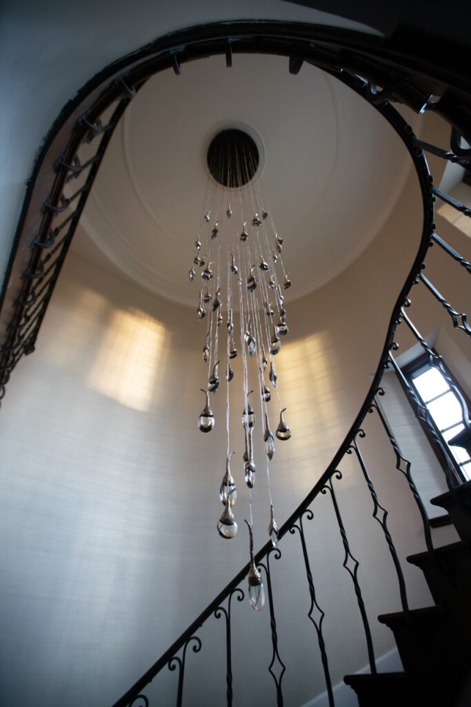 A spiral staircase centers around a long chandelier ceiling piece.