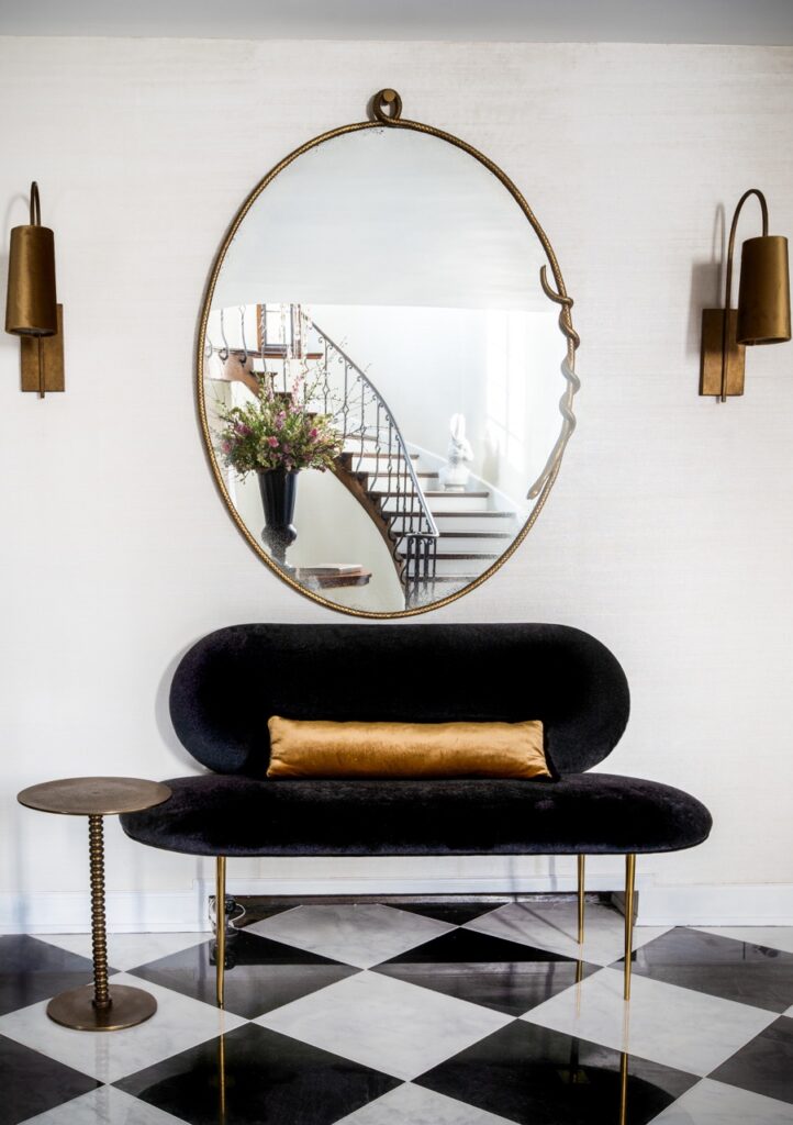 A black couch with a gold pillow sits beneath a mirror with a gold frame.