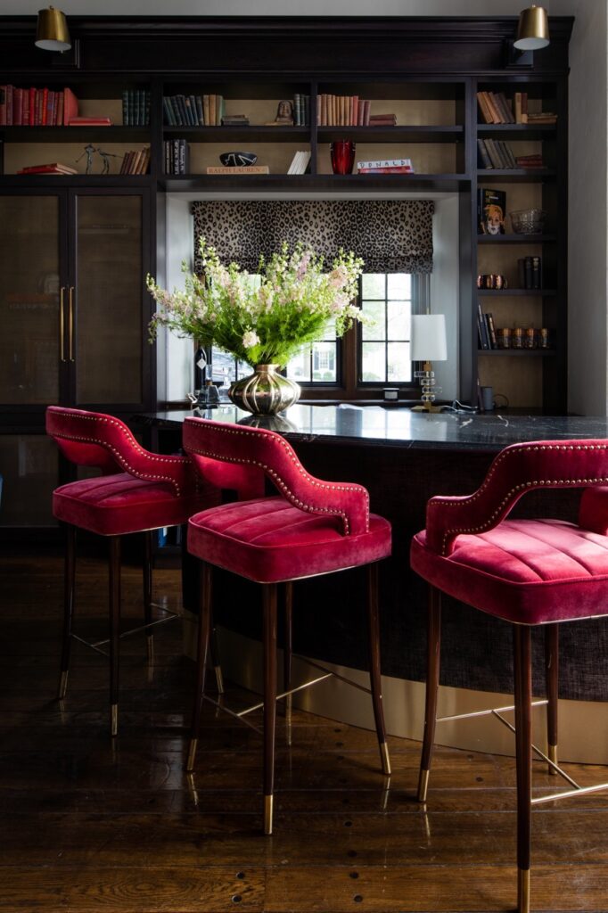 Three hot pink chairs sit against a bar with a vase and greenery arrangement.