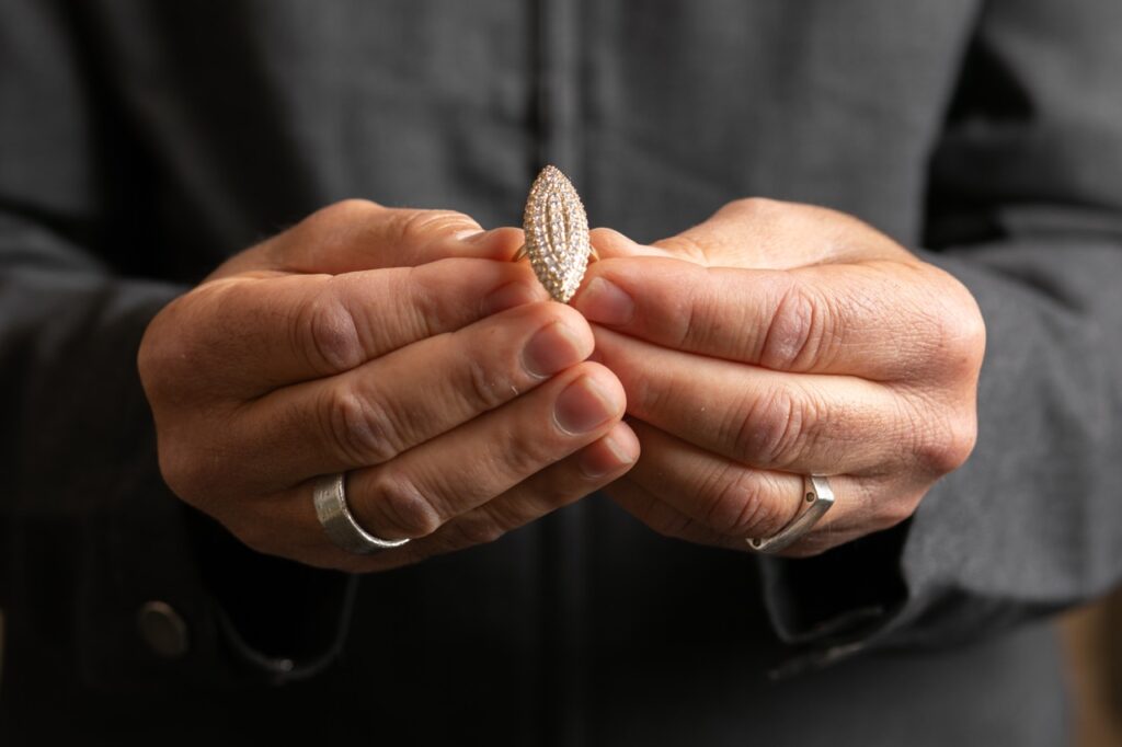 A man holds a diamond ring in an oval shape.