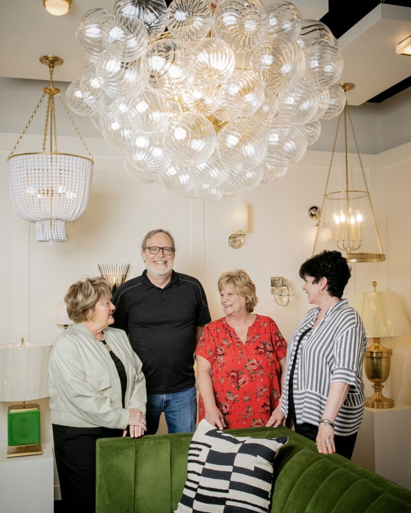 Three women and one man stand under the chandelier light at Cardello lighting and eletric supply.
