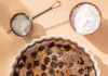 Cherry Clafoutis A white pie dish holds a Cherry Clafoutis with a bowl of powder sugar and a sifter sitting above it.