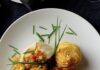 Chilean Sea Bass from LeMont in Pittsburgh Chilean Sea Bass with a Pineapple Mango Chutney sits on a white plate with two sprigs of herbs on top of it.